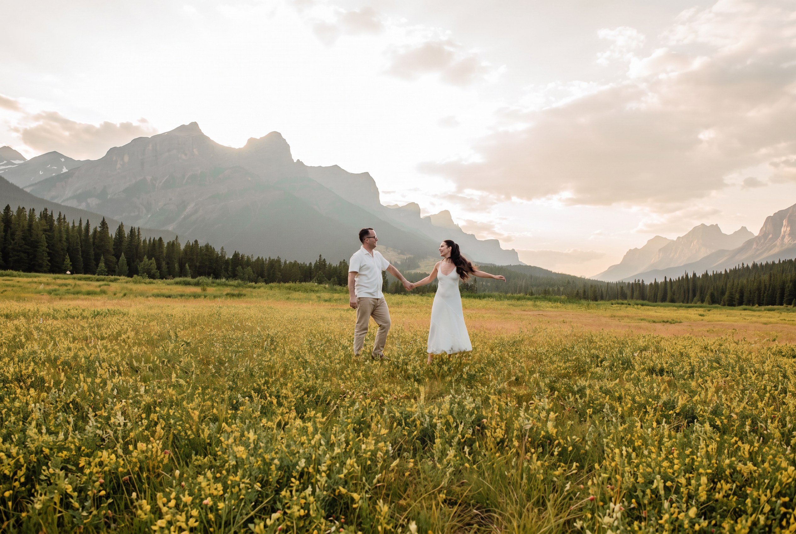Nathalie and David holding hands as they walk through a wildflower meadow with mountains beyond